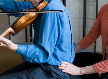 A feldenkrais teacher is helping a violinist find a better way of sitting