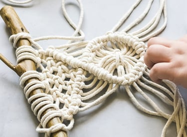 proyecto pequeño de macrame en blanco sobre un tronco de madera