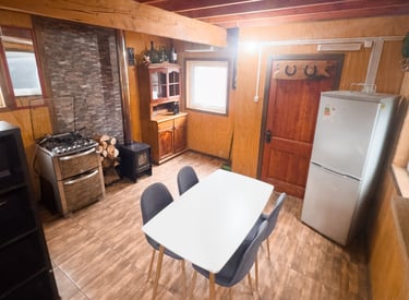 Interior de cabaña rústica equipada en Lonquimay con cocina y calefacción a leña.