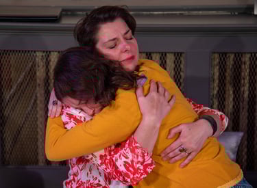 A mother and her preteen daughter embrace tightly, their eyes closed.