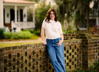 professional portrait of a woman leaning against a brick wall with a house behind her