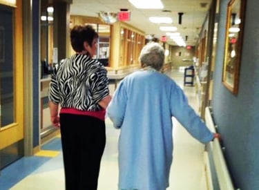 Photo of Debbie escorting her mother down a medical hallway.