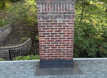 A brick chimney on a brown tiled roof with smoke rising from it, illustrating a safe and active fireplace system