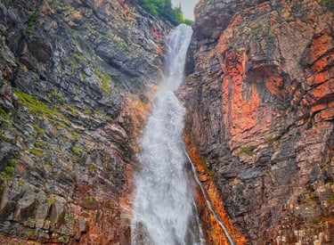 Scenic waterfall cascading down a rugged mountain cliff into a rocky stream in the wilderness.