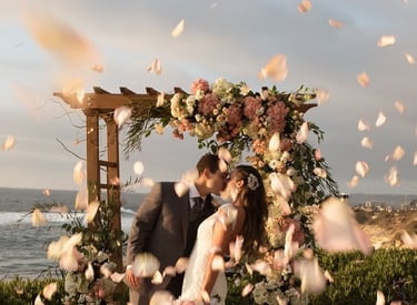 bride and groom kissing in front of a wedding arbor at Cuvier Park pink and white flowers