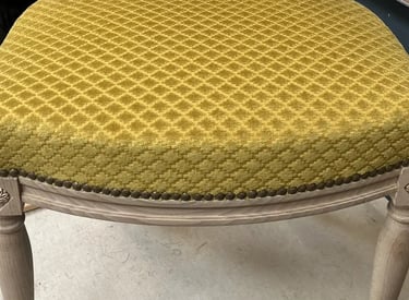Chaise en bois clair recouverte d'un tissu jaune à motifs quadrillés, finit par des clous décoratifs