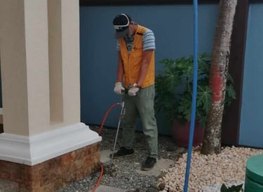Professional pest control technician performing termite soil treatment at a residential home foundation.