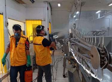 Sanitation workers in safety gear spray disinfectant on a commercial meat processing line for industrial hygiene.