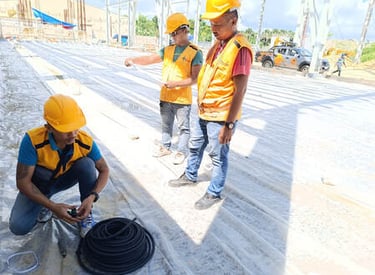 Construction workers in safety gear install a vapor barrier membrane on a building foundation site.