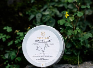 Ygeiax Holy Smoke Ayurvedic herbal mixture tin resting on a stone in a natural garden setting.