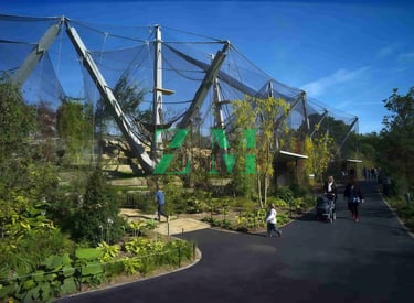 Visitors walk past the Snowdon Aviary walk-through exhibit at London Zoo under a clear blue sky.