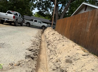 Long trench with trucks and house in background