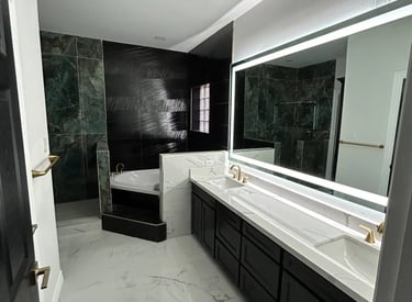 Modern luxury bathroom with double marble vanity, backlit mirror, and a soaking tub with dark tile accents.