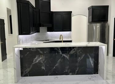 Modern luxury kitchen with black cabinets, white marble floors, and a dark marble waterfall island.