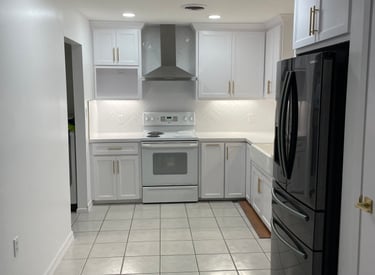 Modern white kitchen with shaker cabinets, gold hardware, and a black refrigerator.