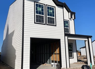 A modern two-story house under construction with white horizontal siding and black window trim.