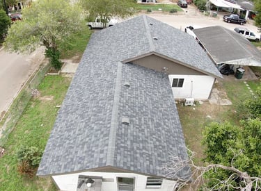 Aerial view of a residential home with new grey architectural asphalt roof shingles and ridge vents.