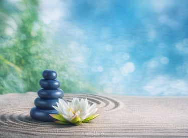 Balanced stack of blue stones beside a white lotus flower on raked sand in a peaceful Zen garden setting