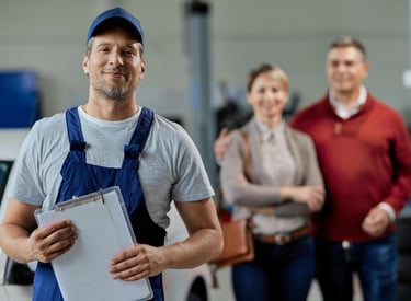 smiling handyman holding a clipboard in an Auckland workshop with clients behind him