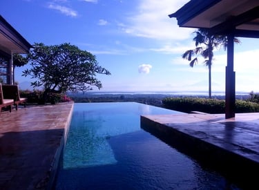 Luxurious infinity pool overlooking a tropical landscape with mountains, ocean, and clear blue sky in Bali.