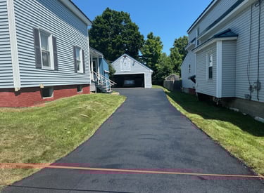 Freshly paved black asphalt driveway between two residential houses leading to a detached garage.