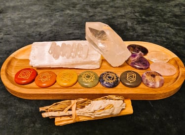A variety of crystals placed on a wooden tray, with bundle of palo santo, sage and rosemary in front