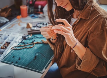Artesana junto a mesa de trabajo con materiales, creando un collar con cuentas