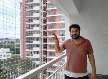 A technician carefully fitting a sturdy pigeon net on a modern apartment balcony in Bellandur.