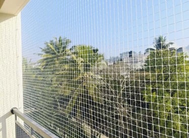Close-up of a sturdy pigeon net installed on a balcony railing with a cityscape in the background.