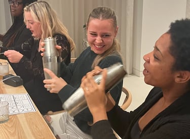 Friends smiling while using cocktail shakers at a professional mixology class event.