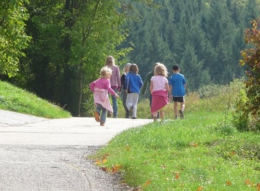 A group of happy children running and walking along a sunny paved path near a green forest.