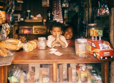 A young child and mother smiling behind the counter of a small local grocery shop.