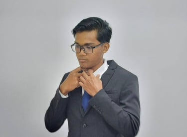 Professional young man in a charcoal suit and blue tie adjusting his collar against a gray background.