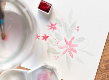 Fotografía que se centra en una ilustración de colores suaves de flores en acuarela se ve también la pastilla de color