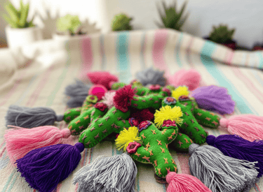 Handmade green felt cactus ornaments with colorful tassels and embroidery on a striped fabric.
