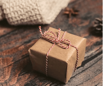 Small brown paper gift box tied with red and white twine on a rustic wooden table.