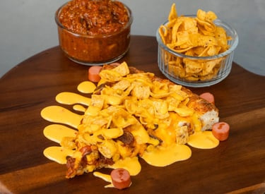 A slice of Bow Tie Pizza's chili cheese dog pizza sitting on a wooden serving board