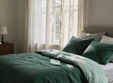 A high-end, serene bedroom in a contemporary North American / US home. Soft sunlight filters through linen curtains onto a bed with organic cotton sheets in deep forest green and light mint colors. The atmosphere is quiet, airy, and trustworthy.
