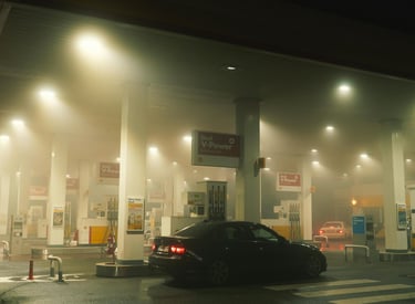 A dimly lit Shell gas station in Chichester, England, with fog or smoke hanging in the air, a black