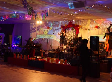 A live band performs on a stage decorated for Dia de los Muertos with colorful papel picado and string lights.