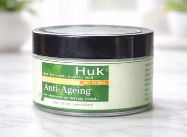 A jar of Huk Anti-Ageing Herbal Cream with hyaluronic acid on a white marble surface.