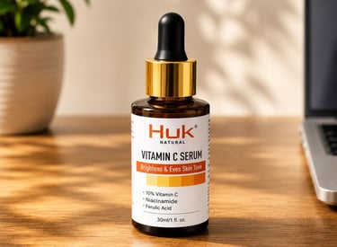 Huk Natural Vitamin C Serum bottle with niacinamide and ferulic acid on a wooden desk near a plant.