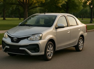 Toyota Etios 2015 prateado estacionado em avenida arborizada, com grama e árvores ao fundo sob luz n