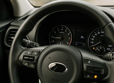 Painel de carro com luz de combustível acesa e autonomia baixa, visto do volante em primeiro plano.