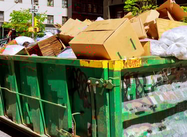 alt="Green dumpster overflowing with cardboard boxes and household junk during property cleanout"