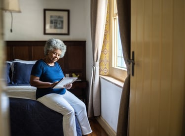 Senior woman sitting on a bed looking back at a photo of a loved one with quiet reflection