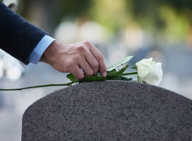 Suited hand neatly placing a single white rose on a gravestone symbolizing urgent remembrance