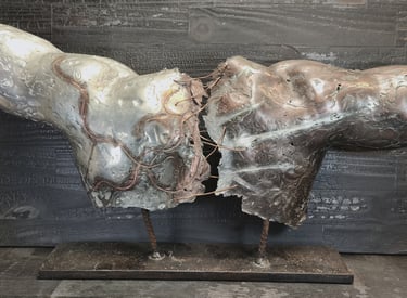 Abstract metal torso sculpture with oxidized copper details on a charred wood background.