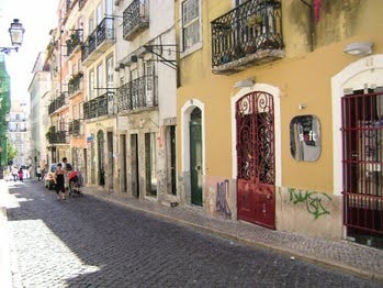 Lisbon - row of apartments & businesses with doors & false balconies facing the cobblestone street