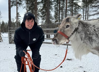 a smiling man in a black jacket next to a reindeer